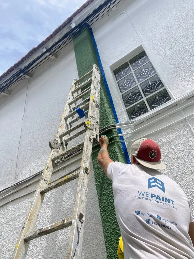 Pintor de WePaint pintando el frente de una casa sobre escalera